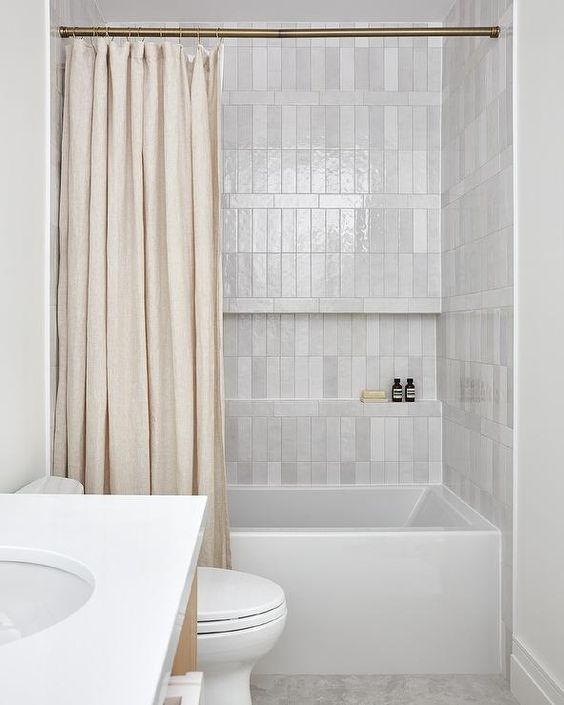 a neutral bathroom clad with white and grey stacked tiles, with white appliances and a neutral shower curtain is cool