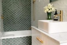 a neutral bathroom with a white planked vanity and a sink, a bathing space done with green fishscale tiles and gold fixtures