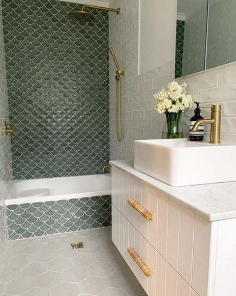 a neutral bathroom with a white planked vanity and a sink, a bathing space done with green fishscale tiles and gold fixtures