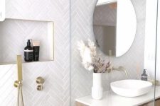a neutral bathroom with white herringbone tiles, a stained vanity and a bowl sink, a round mirror and gold fixtures