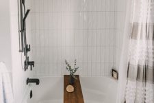 a neutral bathroom with white stacked tiles around the tub, black penny tiles on the floor, a printed curtain and black fixtures