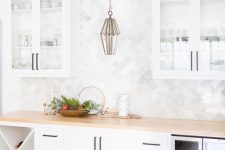 a neutral farmhouse kitchen with white cabinets, a wooden countertop and a marble tile backsplash plus a catchy pendant lamp