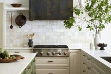 a neutral kitchen with a green kitchen island, a white Zellige tile backsplash and a darkened metal hood