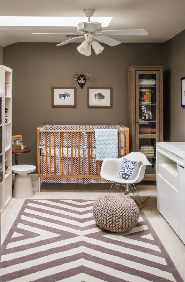 a nursery with brown walls, a couple of storage units, a stained crib, a white changing table, a printed rug and some poufs
