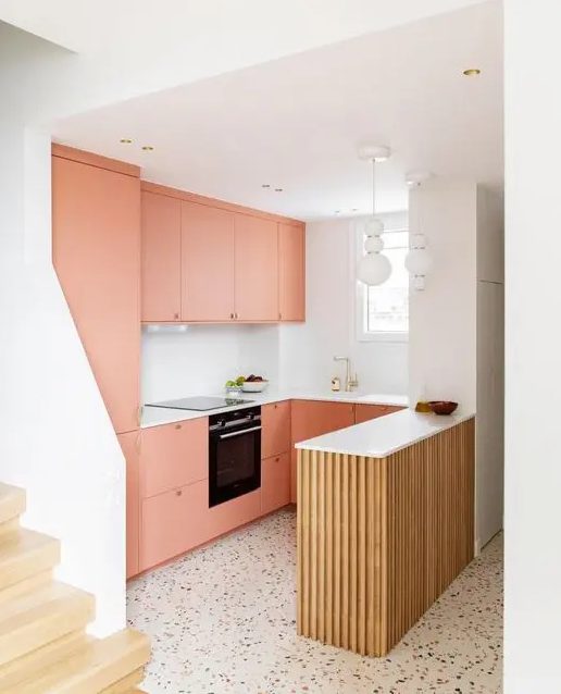 a peachy kitchen with a fluted kitchen island, a white backsplash and countertops, white pendant lamps