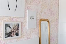 a pink bedroom with floral wallpaper, a white bed and pink and white bedding, some art and a mirror in a gold frame