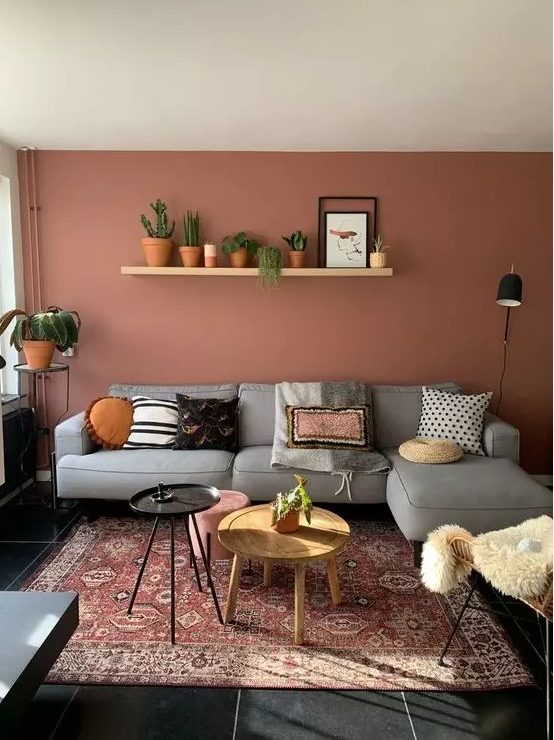 a pretty boho living room with a terracotta statement wall, a grey sectional, a rattan chair and some potted plants and round tables