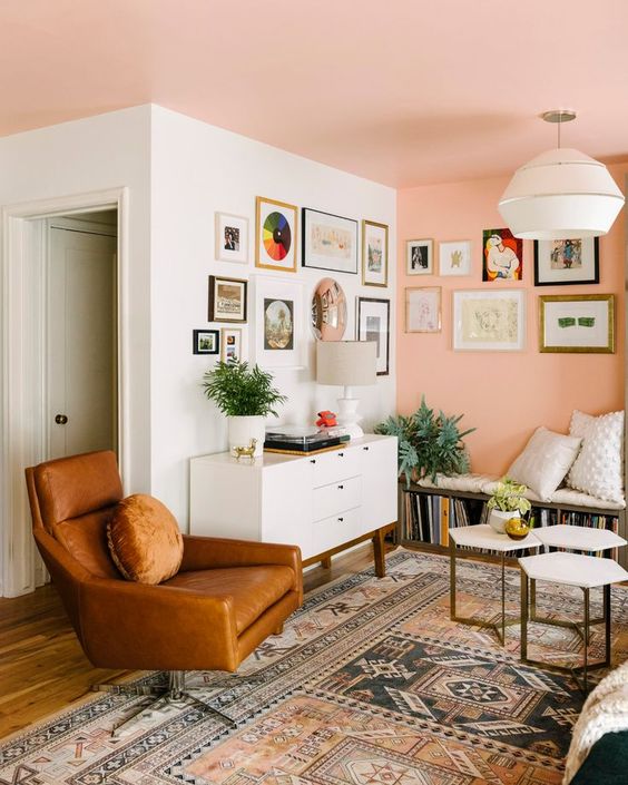 A pretty mid century modern living room with a Peach Fuzz wall and ceiling, a bench with books, a white credenza, a leather chair