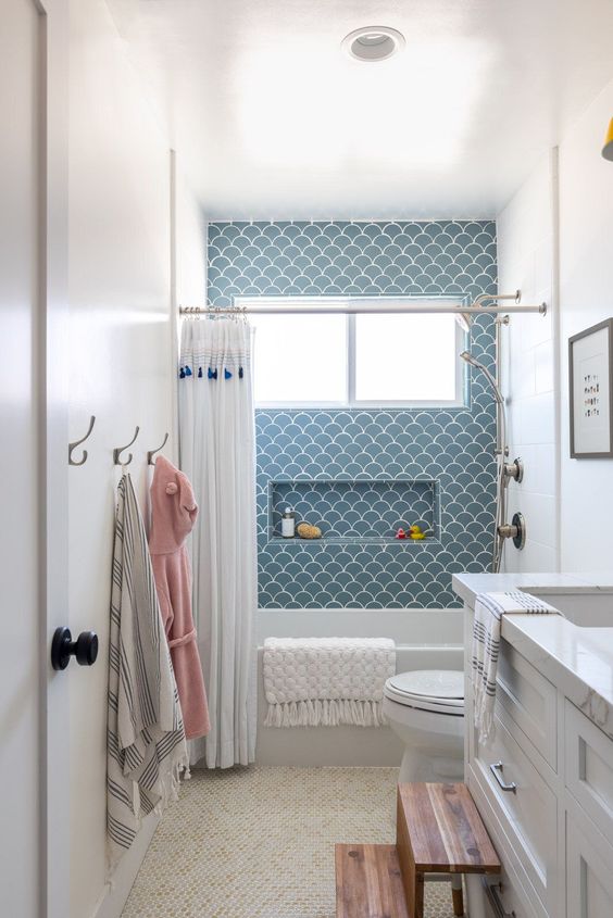 a pretty small bathroom in neutrals, with a blue scallop accent wall, a white vanity, a stool and some textiles