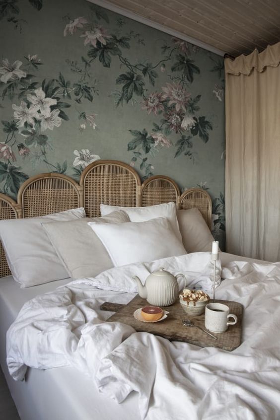 a refined bedroom with green floral wallpaper, a bed with a rattan headboard, neutral bedding is a cool and chic space