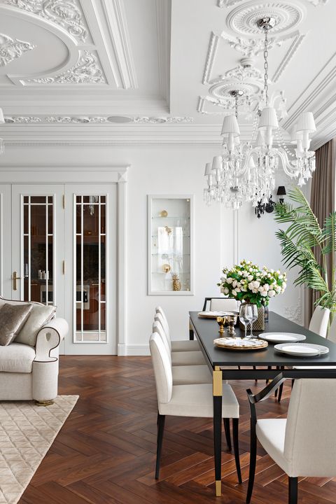 A refined living and dining room with a beautiful ceiling, dark stained herringbone floors, a black table and white chairs