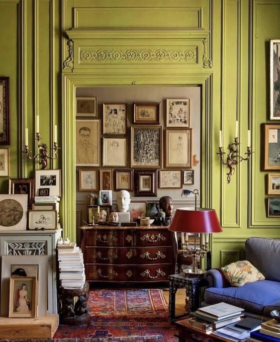 a refined space with chartreuse paneled walls, a rich-stained dresser, a gallery wall, a blue chair and some lamps