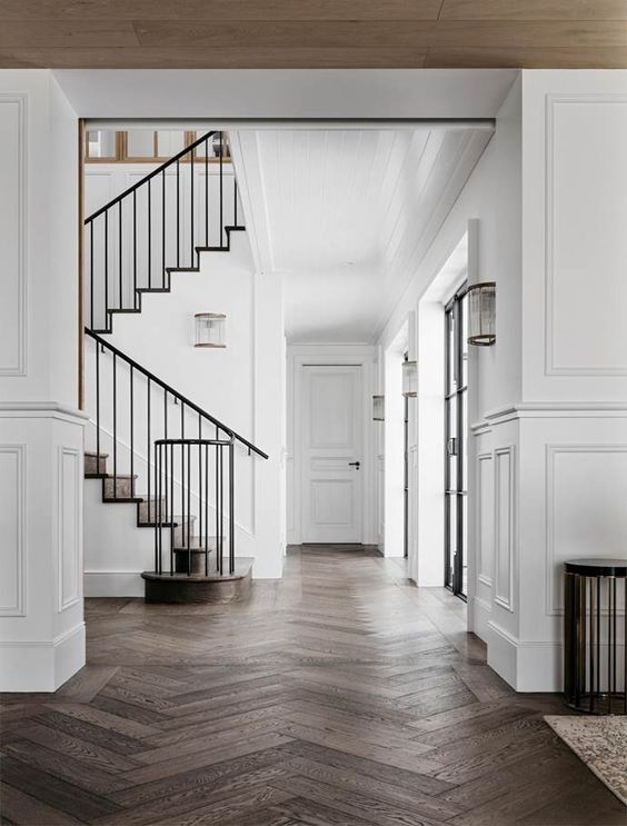 A refined space with white walls with molding and dark stained herringbone floors, black railing is super chic