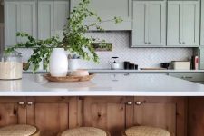 a sage green kitchen with shaker style cabinets, a herringbone tile backsplash, a stained kitchen island with a white countertop