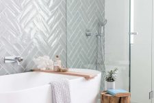 a serene Scandinavian bathroom with a grey herringbone tile wall, a shower, an oval tub and a wooden stool