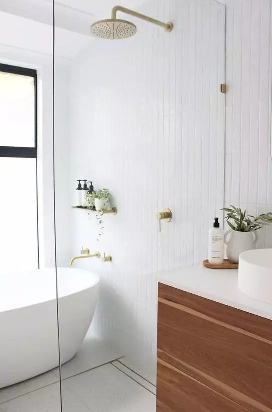a serene Scandinavian bathroom with white stacked tiles, a stained timber vanity, an oval tub and gold fixtures
