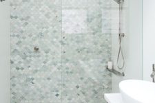 a serene bathroom done with large scale tiles and aqua and green fishscale tiles in the shower, a stained vanity