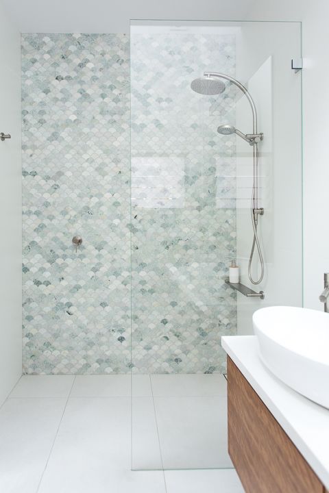 a serene bathroom done with large scale tiles and aqua and green fishscale tiles in the shower, a stained vanity
