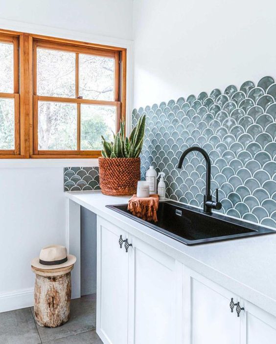 a serene white kitchen with shaker cabinets, white stone countertops, a grey fish scale tile backsplash, black fixtures