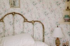a shabby chic bedroom with delicate floral wallpaper, a shabby chic bed, floral bedding, a stool as a nightstand and a vintage lamp