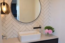 a sink zone with white herringbone tile, a built-in vanity, a round mirror and a pendant lamp is a cool and minimal space
