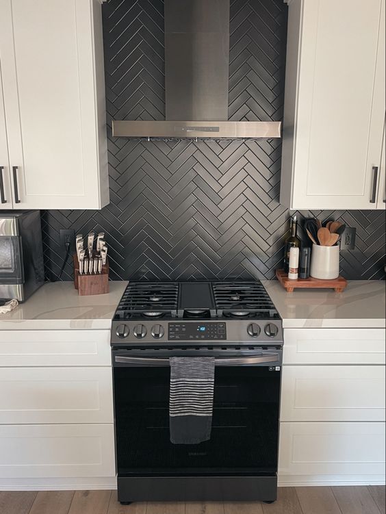 a sleek white kitchen with shaker cabinets, a black herringbone tile backsplash, black appliances and white marble countertops