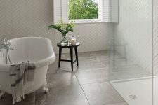 a small attic bathroom with herringbone and large format tiles, a clawfoot tub, a shower space, shutters and a black stool