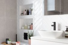 a small neutral bathroom with white herringbone tiles, grey stone ones, a white vanity, a mirror cabinet and niche shelves
