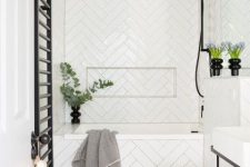a small white bathroom done with herringbone tiles, a free-standing vanity, black fitures and greenery