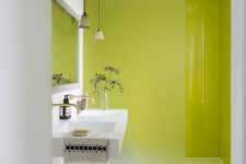 a small yet bold bathroom with chartreuse walls in the shower, an iced glass divider, a floating sink, a neutral rug and pendant lamps