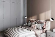a sophisticated bedroom with a taupe accent wall and a matching accented ceiling, a neutral bed and taupe and grey bedding, a sleek wardrobe and nightstands