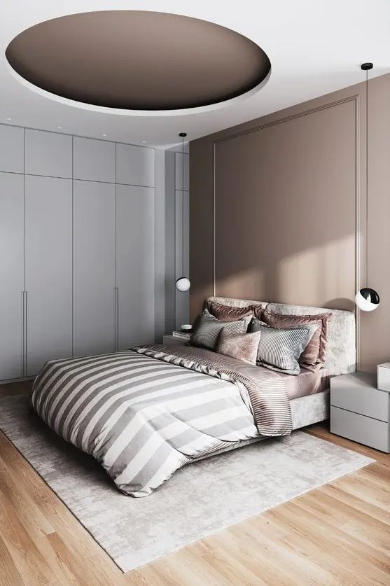 a sophisticated bedroom with a taupe accent wall and a matching accented ceiling, a neutral bed and taupe and grey bedding, a sleek wardrobe and nightstands
