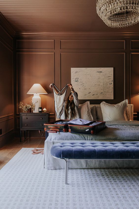 a sophisticated bedroom with molding, a neutral bed with blue bedding and a bench, nightstands and a crystal chandelier