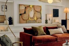 a sophisticated earthy tone living room with a burgundy sofa and pillows, a creamy boucle chair, a colorful rug, eye-catchy decor