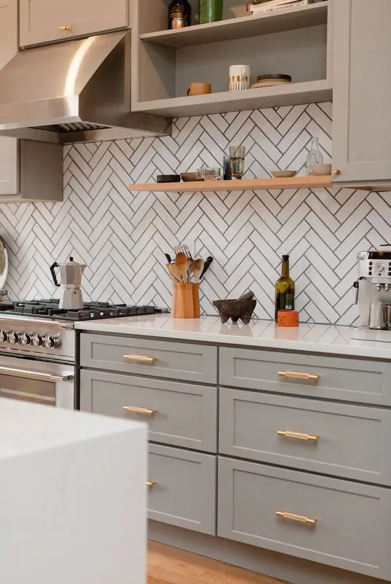 a sophisticated light grey kitchen with shaker cabinets, a white chevron tile backsplash, white countertops and a shiny metal hood