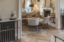 a sophisticated neutral space with light-stained herringbone floors, neutral seating furniture, a fireplace and some lamps