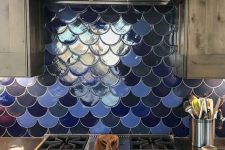 a stained kitchen with blue and a navy fishscale tile backsplash, dark countertops and stainless steel appliances