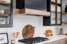 a stained wood kitchen with upper black glass cabinets, a black wood clad hood and white countertops