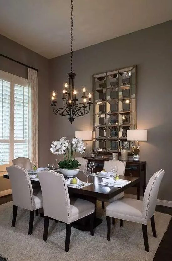 A stylish and exquisite taupe dining room with a dark stained table and a credenza, neutral chairs, a black vintage chandelier and a mirror piece on the wall