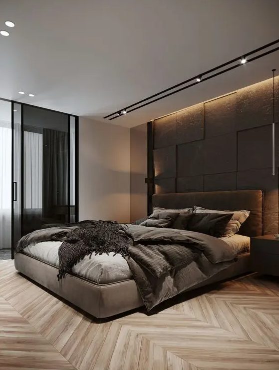 A stylish and refined modern bedroom with a taupe accent wall, a taupe upholstered bed with matching bedding, built in lights and glass sliding doors