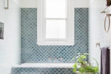 a stylish bathroom clad with white tiles and with navy fishscale ones around the bathtub plus a potted plant is a cool space