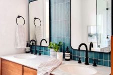 a stylish bathroom with a blue tile stacked wall, a stained vnaity, mirrors, black fixtures and some lamps