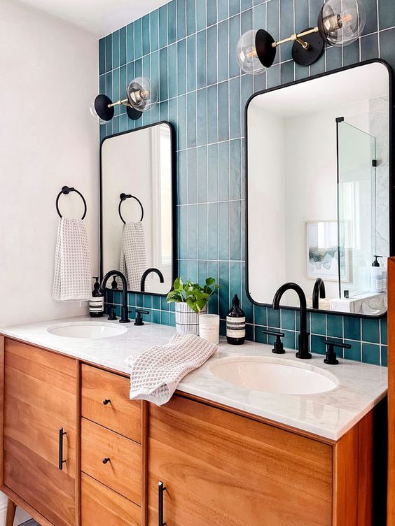 a stylish bathroom with a blue tile stacked wall, a stained vnaity, mirrors, black fixtures and some lamps