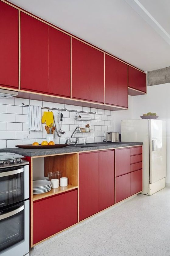 A stylish bold mid century modern kitchen with red plywood cabinets and a white subway tile backsplash and a white fridge