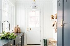 a stylish farmhouse mudroom with navy cabinetry and a herringbone tile floor, a bench and some baskets