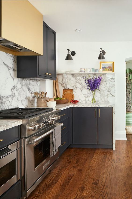 a stylish graphite grey kitchen with white stone countertops and a backsplash, a gold hood for an accent is wow