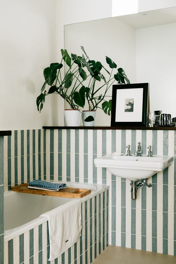 a stylish green and white bathroom done with stacked tiles, with a all-mounted sink, a large mirror and some decor