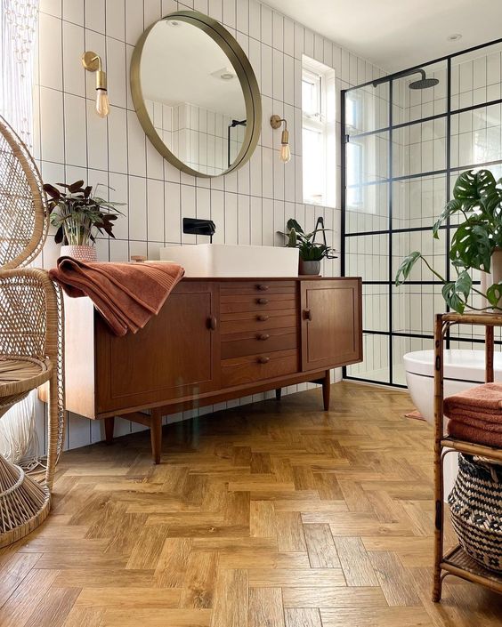 A stylish mid century modern bathroom with white skinny tiles and a herringbone floor, a stained vanity, a papasan chair and a shower