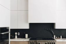 a stylish minimalist kitchen with light stained cabinets, white upper ones, a matte black herringbone backsplash and white quartz countertops