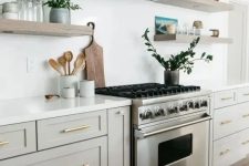 a stylish neutral kitchen in creamy and dove grey cabinets, wooden floating shelves and a white hood